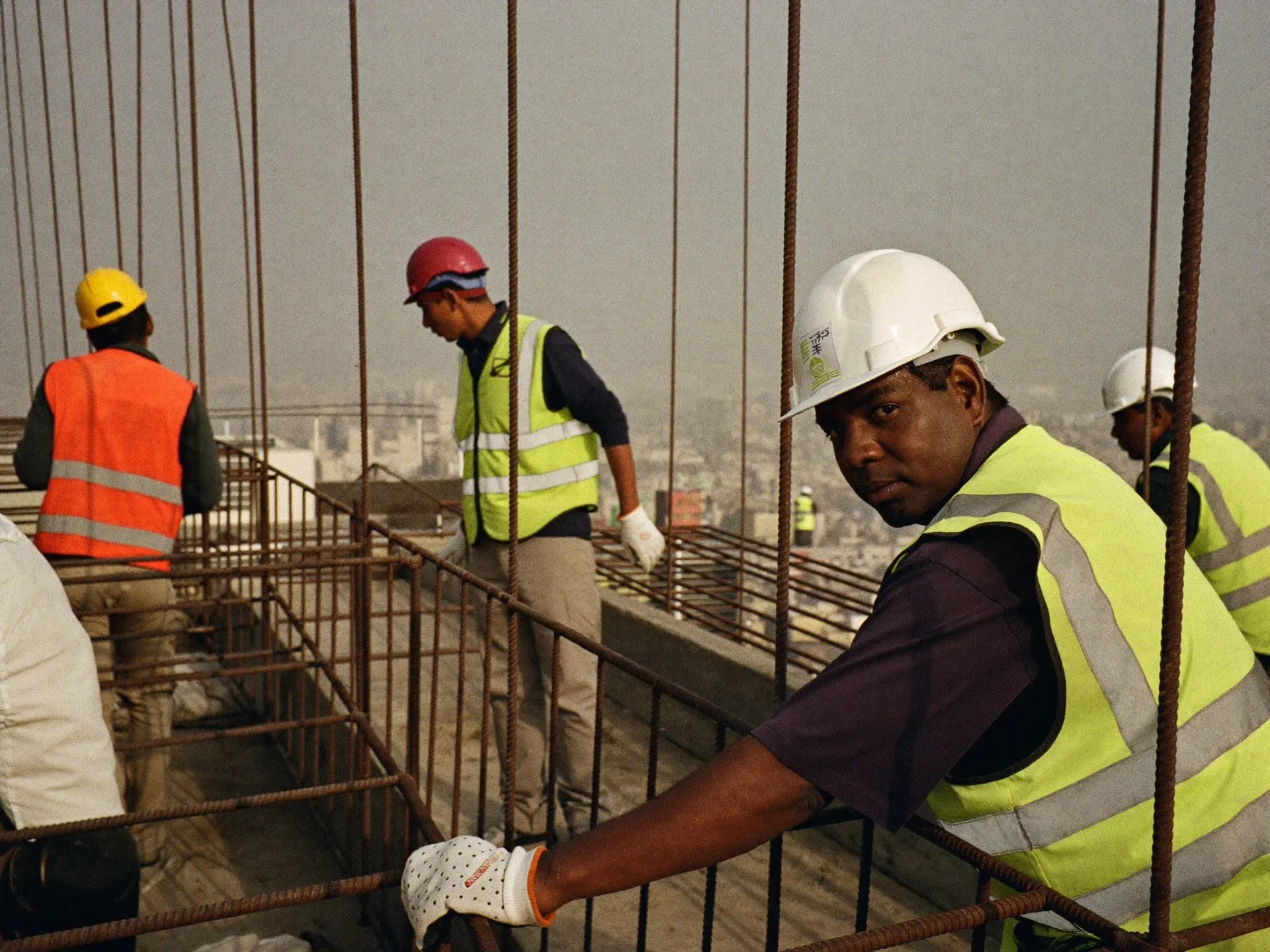 Indian construction workers in helmets and hi-vis vests on a steel frame at a building site