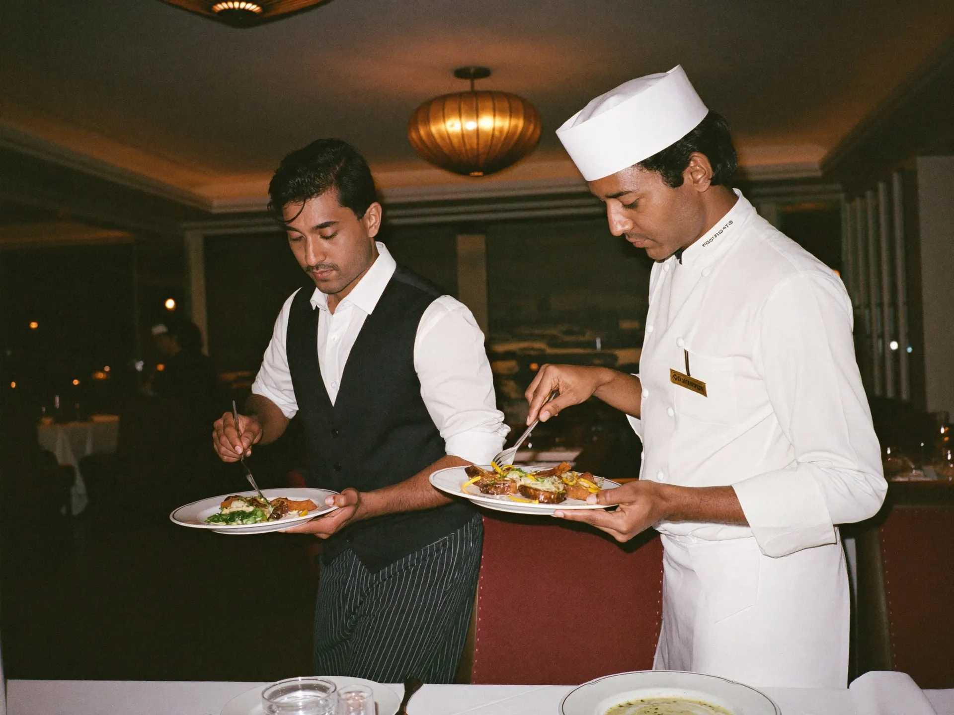 An Indian chef plating a dish in a busy hotel kitchen