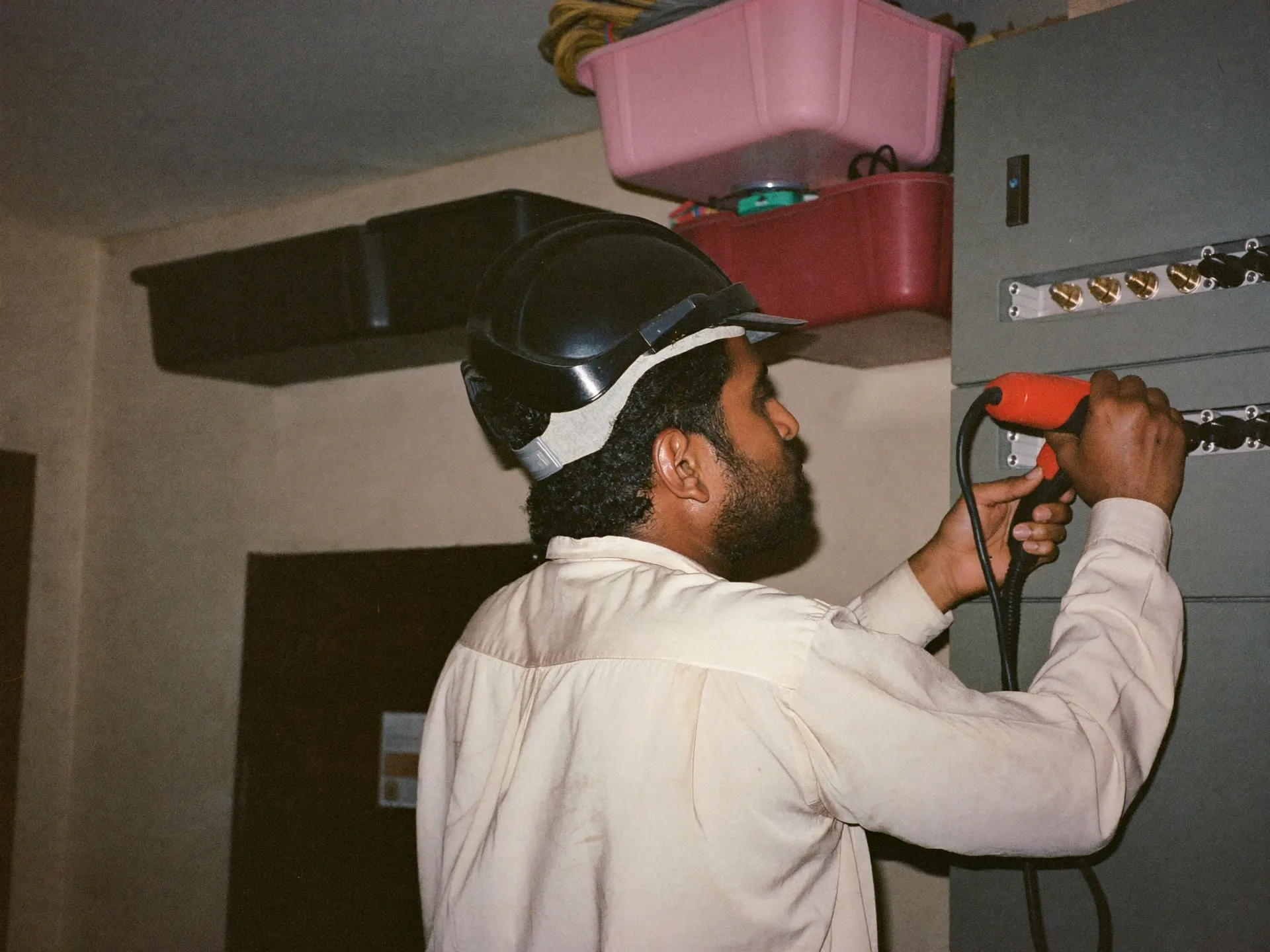An Indian maintenance technician testing an electrical panel with a multimeter