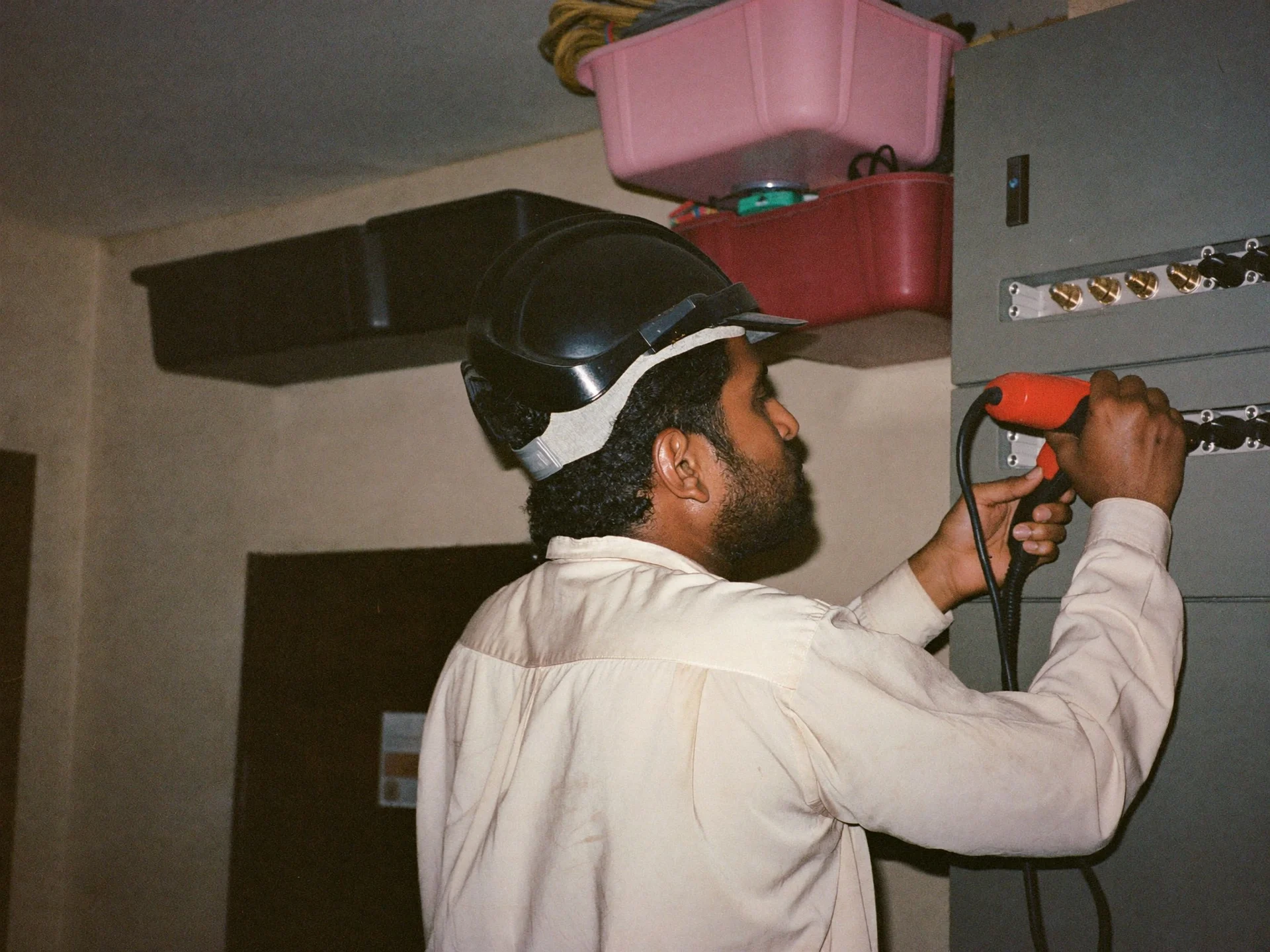 An Indian maintenance technician testing an electrical panel with a multimeter